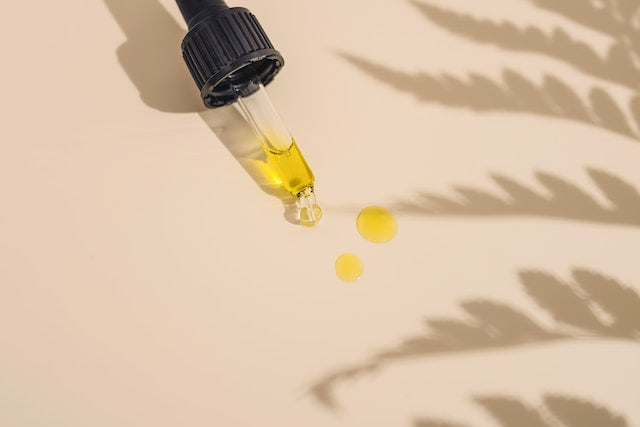 A small glass dropper bottle of CBD oil placed beside a hemp leaf and a pain relief journal on a wooden table.