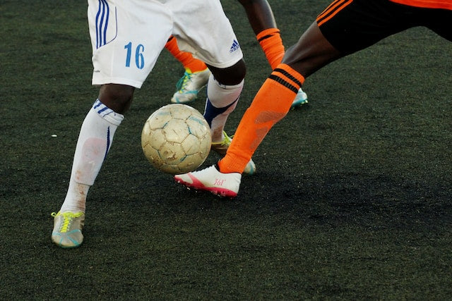 Premier League football players performing strength and agility drills on a training pitch with cones and resistance bands.